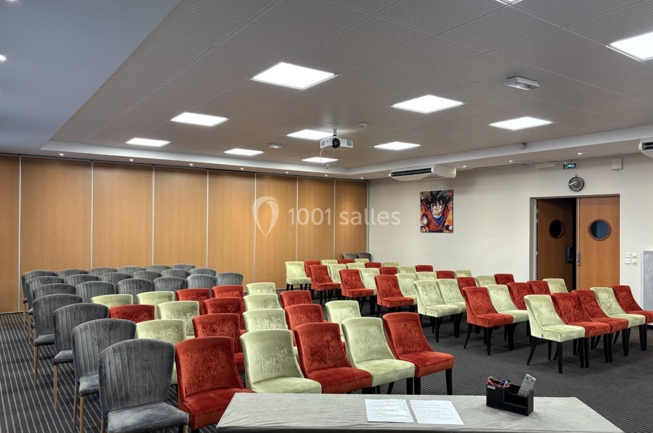 Salle de conférence moderne avec rangées de chaises colorées, éclairage au plafond et équipement audiovisuel.