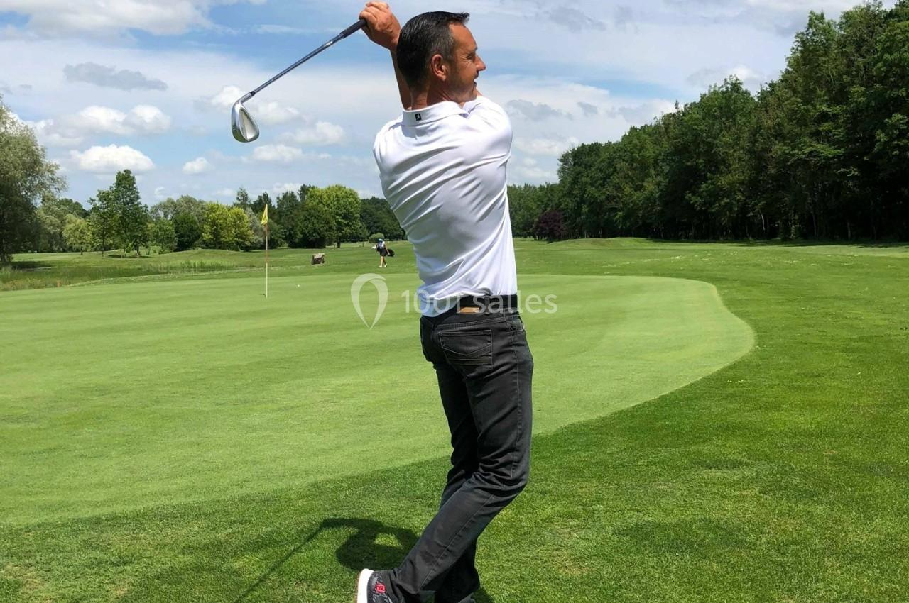 Un golfeur effectue un swing sur un terrain verdoyant par temps ensoleillé.