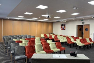 Salle de conférence avec rangées de chaises colorées, un pupitre à l'avant et des panneaux en bois en arrière-plan.