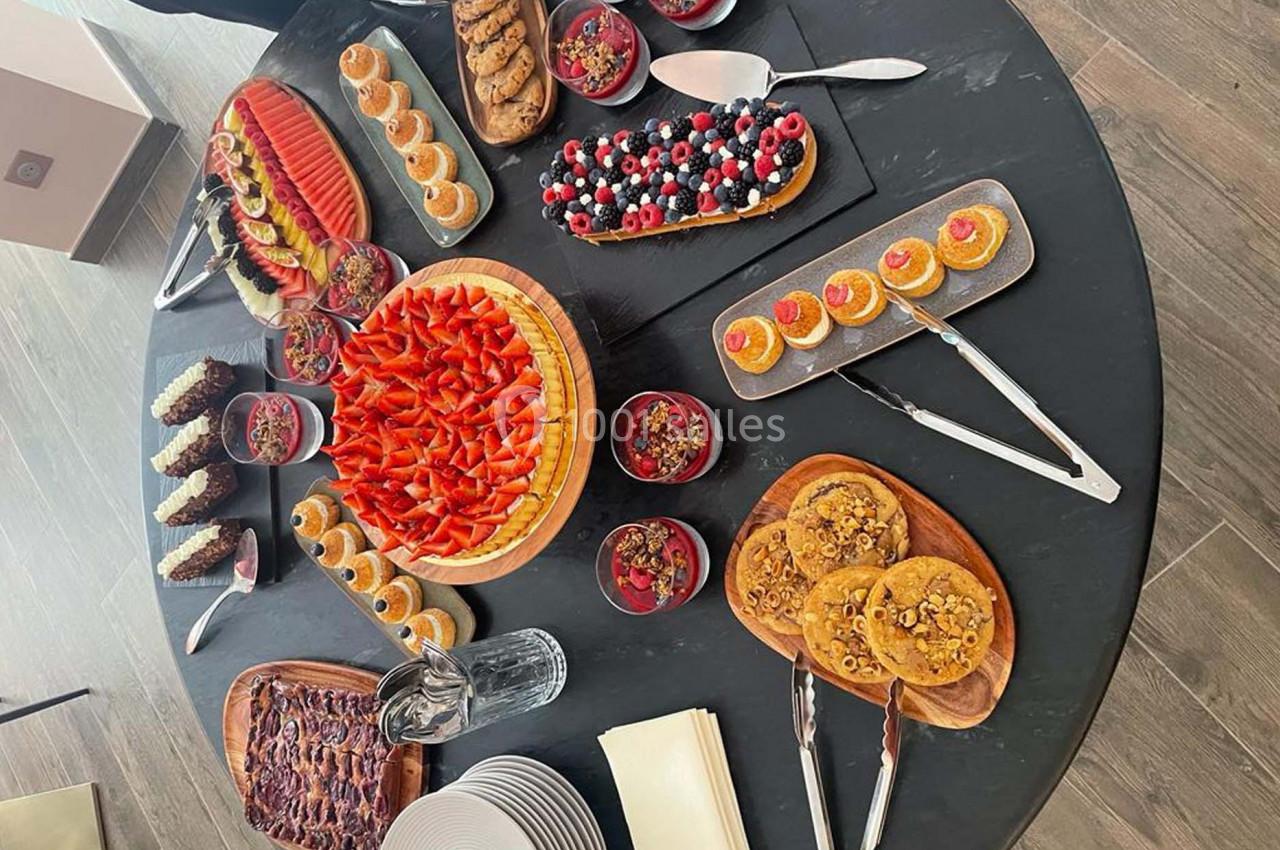 Table ronde garnie de desserts variés : tartes aux fruits, verrines, biscuits et pâtisseries, avec assiettes et serviettes à…