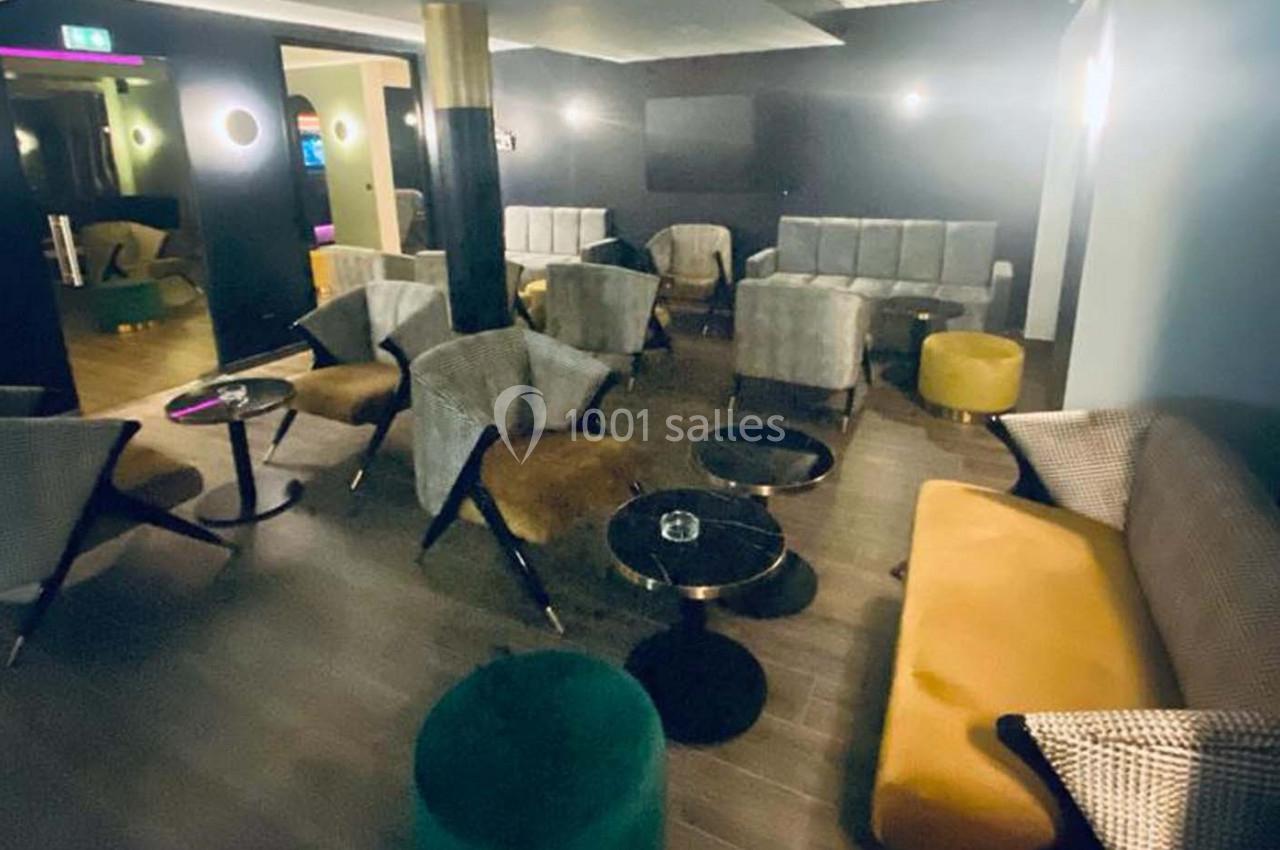 Salon moderne avec fauteuils, canapés, tables basses et éclairage tamisé dans une ambiance conviviale.