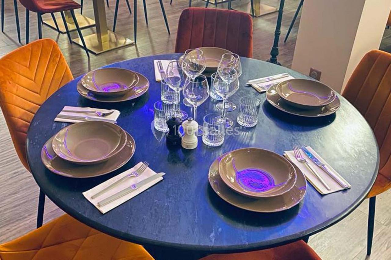 Table ronde dressée avec vaisselle, verres et couverts, entourée de chaises rembourrées dans un restaurant moderne.