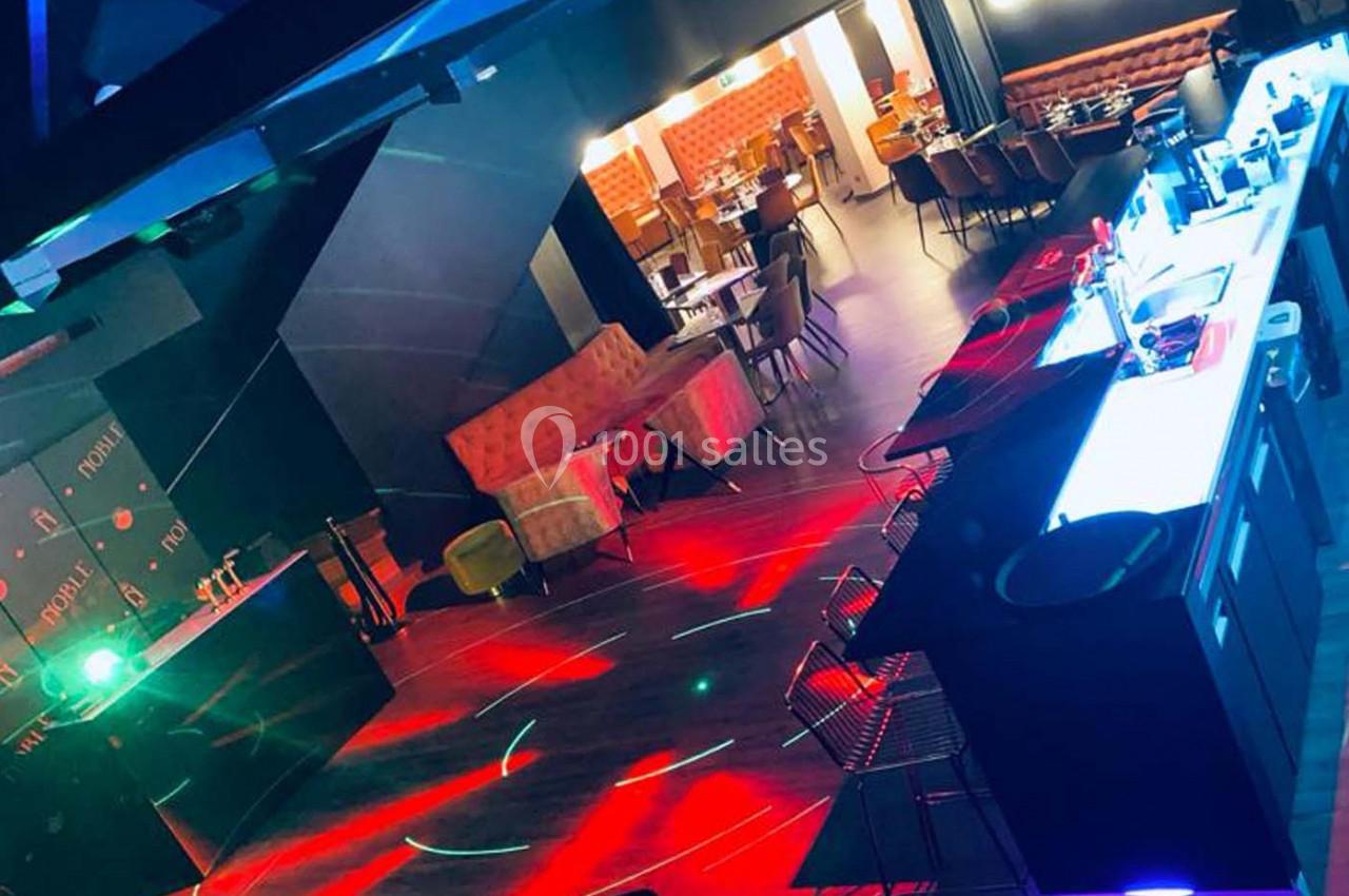 Salle de bar et restaurant avec éclairage coloré, tables dressées et espace ouvert pour des événements.