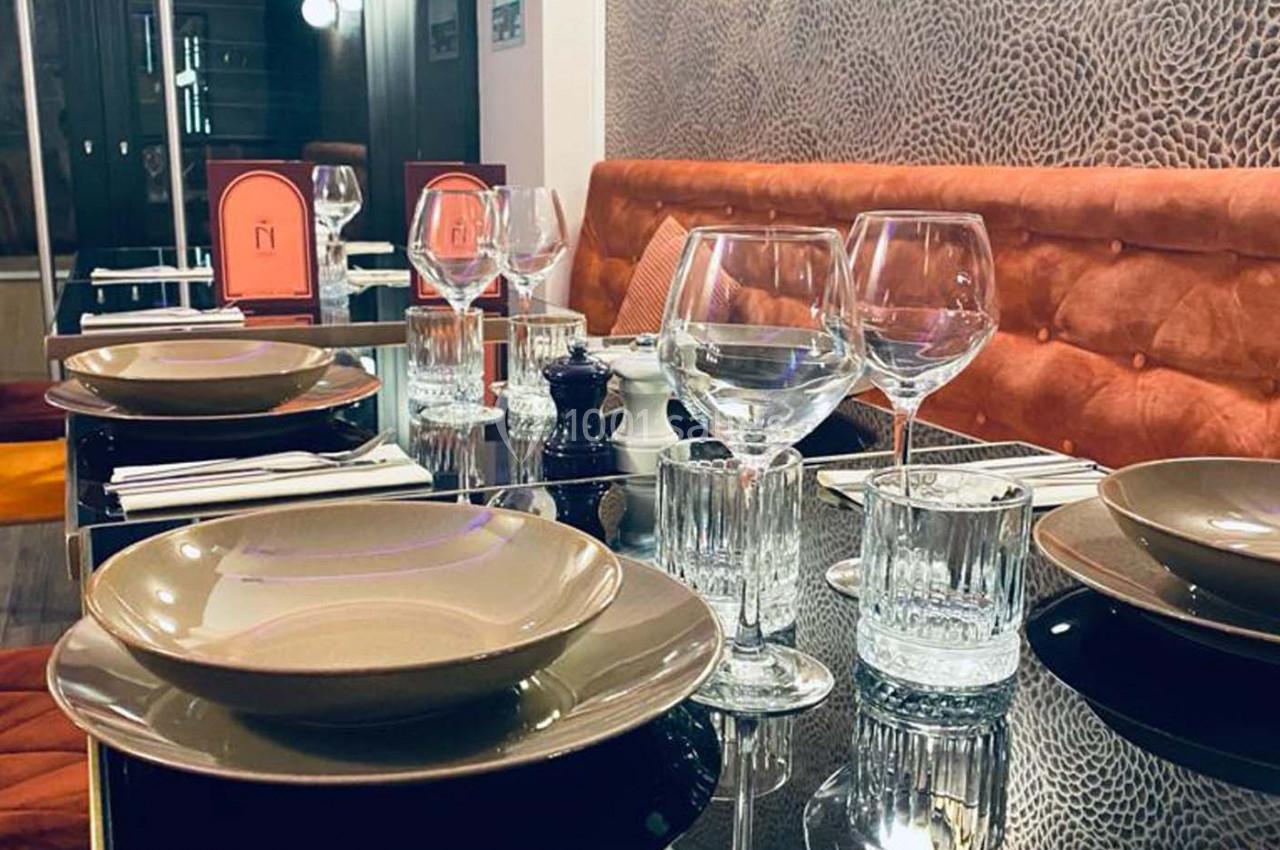 Table dressée avec vaisselle élégante, verres et serviettes sur une surface noire brillante, banquette orange en arrière…