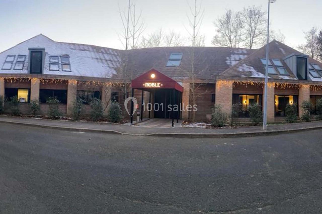 Bâtiment en briques avec toit enneigé, décoré de guirlandes lumineuses, entouré d'arbres en hiver.