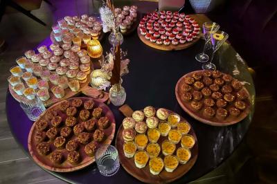 Table garnie de desserts variés, incluant une pièce montée, des verrines et des pâtisseries, dans un cadre tamisé.