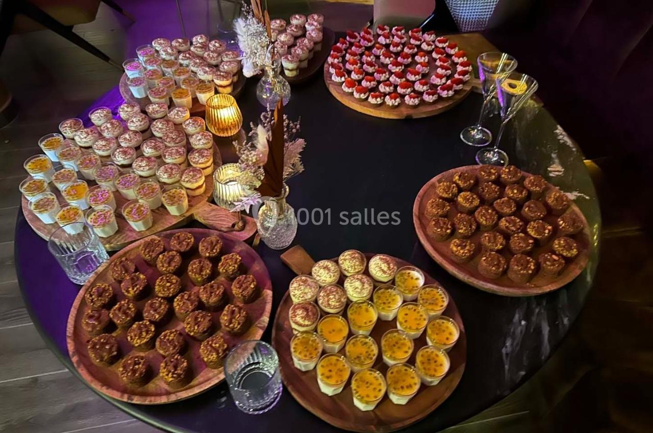 Table ronde garnie de petits desserts variés, disposés sur des plateaux en bois, éclairée par une lumière tamisée.