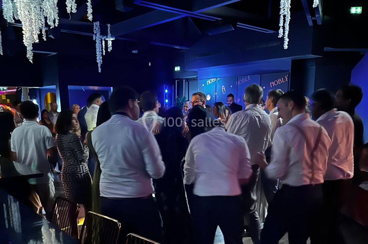 Des personnes dansent et discutent dans une salle sombre éclairée par des lumières colorées, ambiance festive.