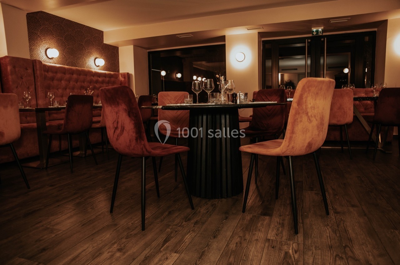Salle de restaurant élégante avec chaises en velours, tables dressées et éclairage tamisé.