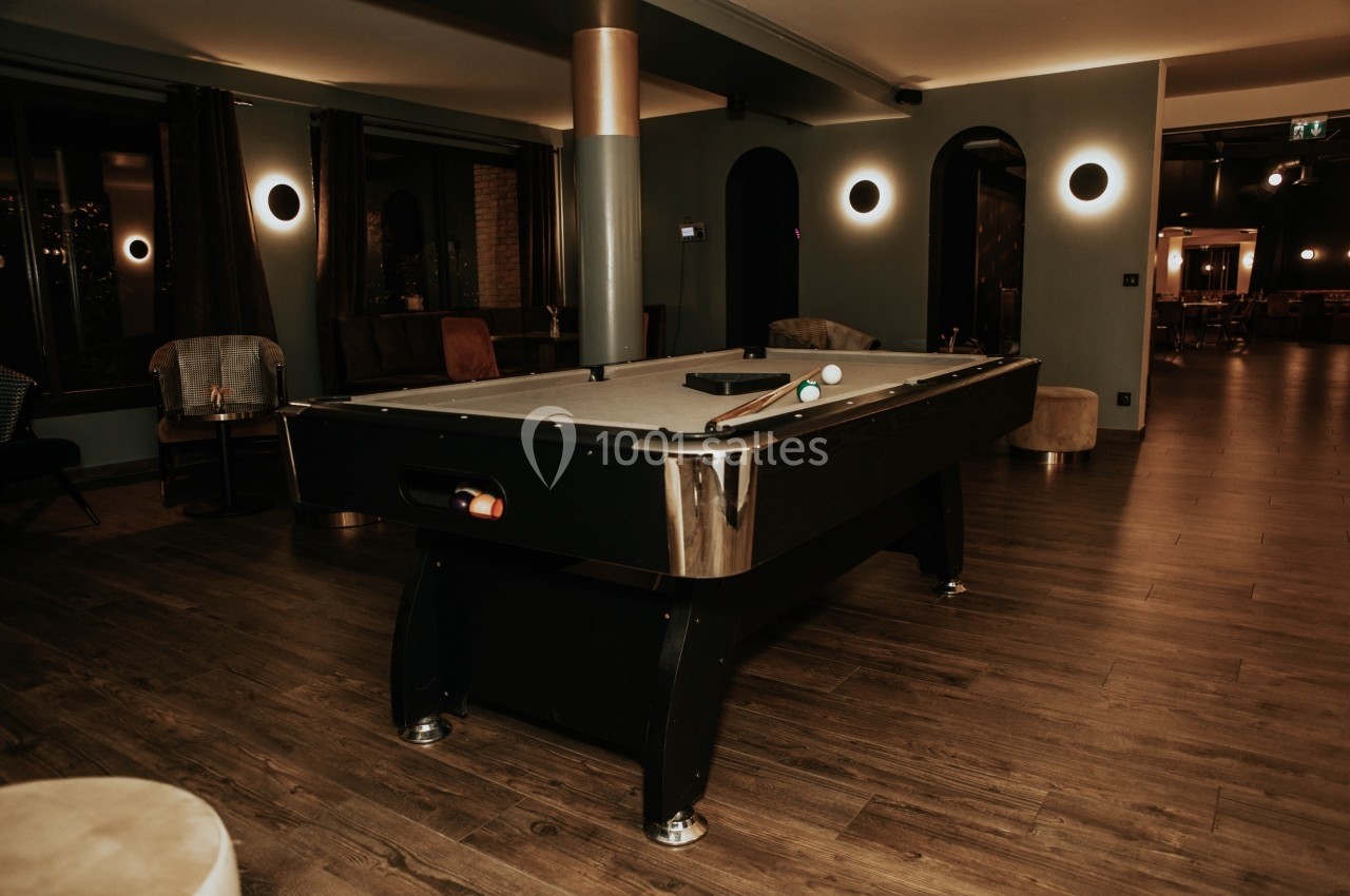 Table de billard noire dans une pièce chaleureuse avec éclairage tamisé et parquet en bois.