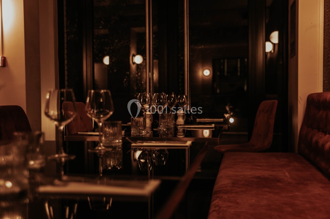 Salle de restaurant élégante avec éclairage tamisé, tables dressées et banquettes en velours rouge.