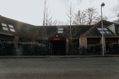Terrasse extérieure avec tables et chaises noires, entourée de végétation et de bâtiments résidentiels.