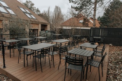 Terrasse extérieure avec tables et chaises noires, entourée de végétation et de bâtiments résidentiels.