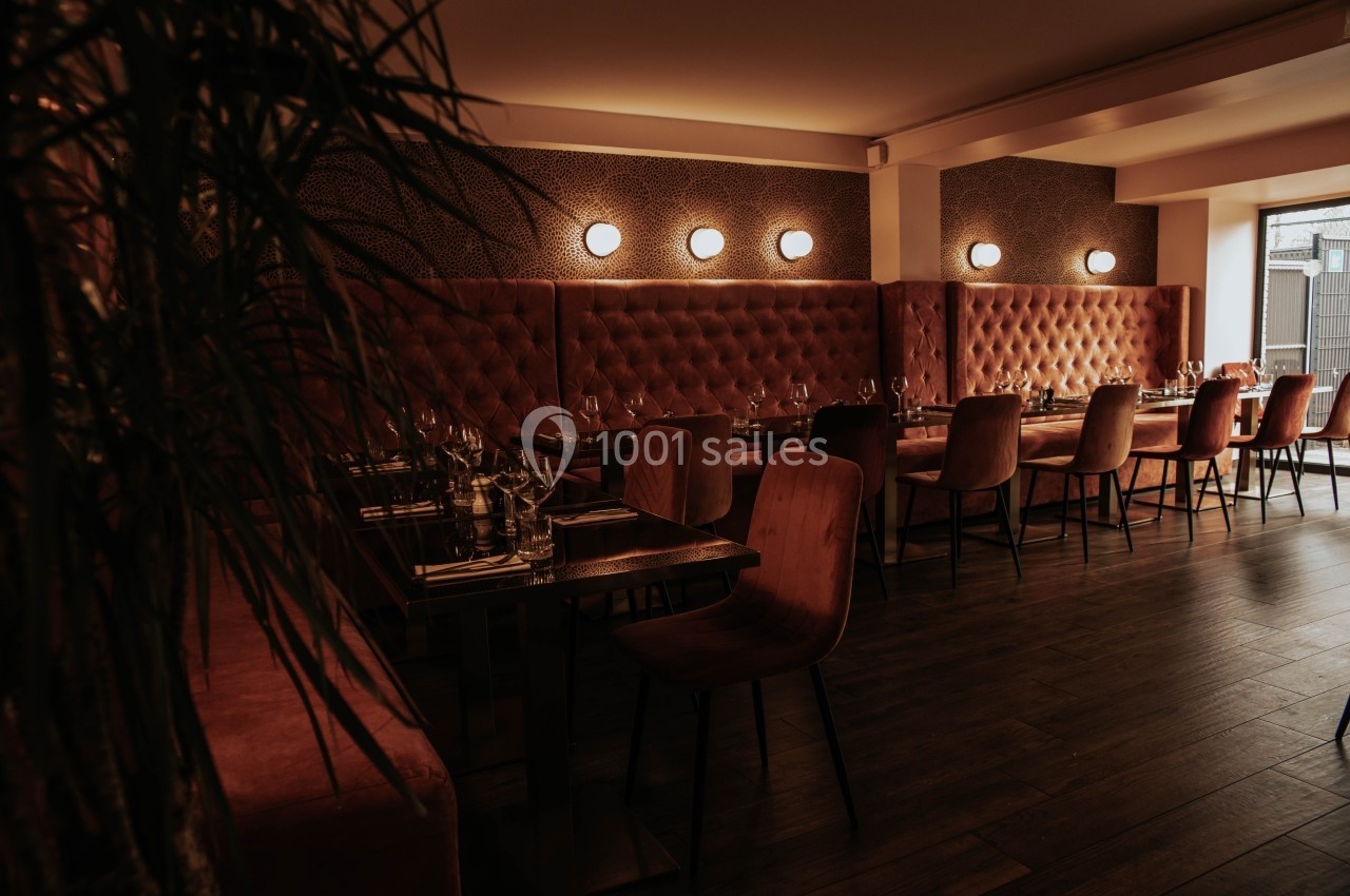 Salle de restaurant chaleureuse avec banquettes capitonnées rouges, chaises en bois et éclairage tamisé.