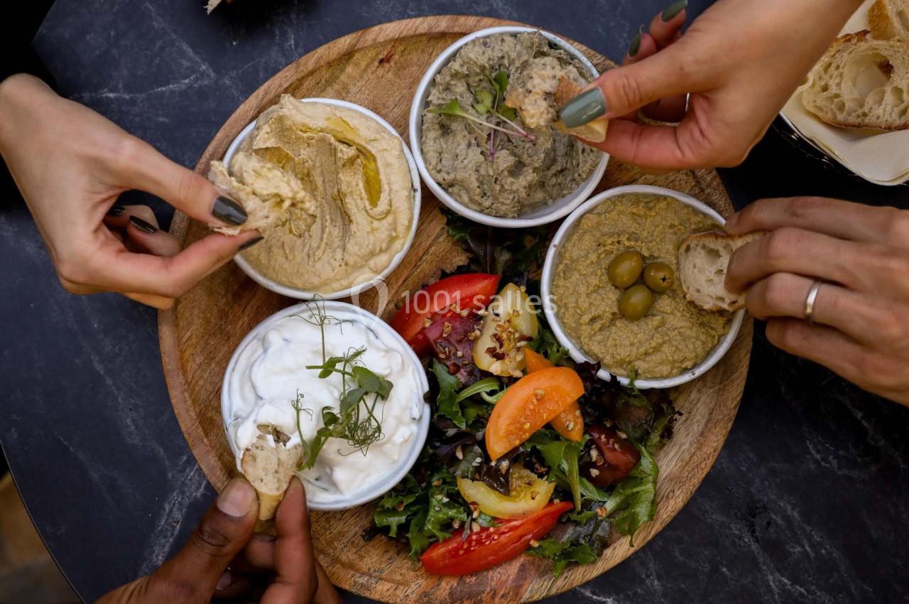 Assiette ronde avec houmous, caviar d’aubergine, tzatziki, salade et mains prenant des morceaux de pain.