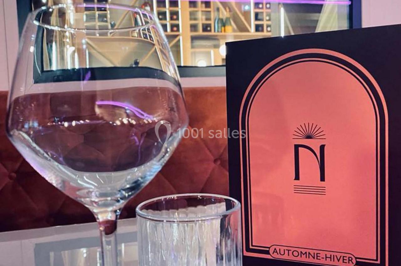 Un verre à vin, un verre d'eau et une carte de menu ’Automne-Hiver’ posés sur une table dans un cadre élégant.