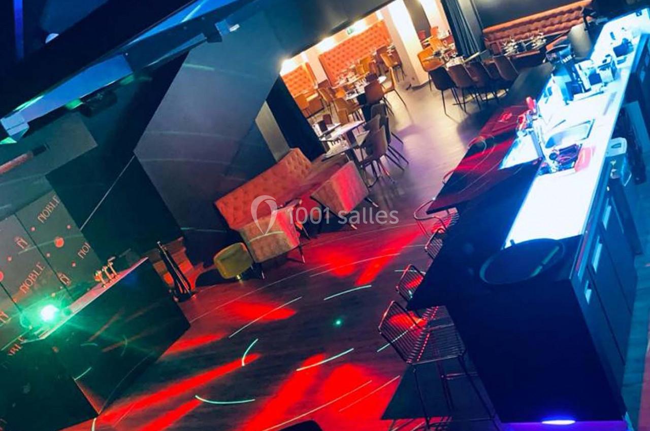 Salle de bar ou restaurant avec éclairage coloré, tables disposées et un comptoir lumineux au premier plan.