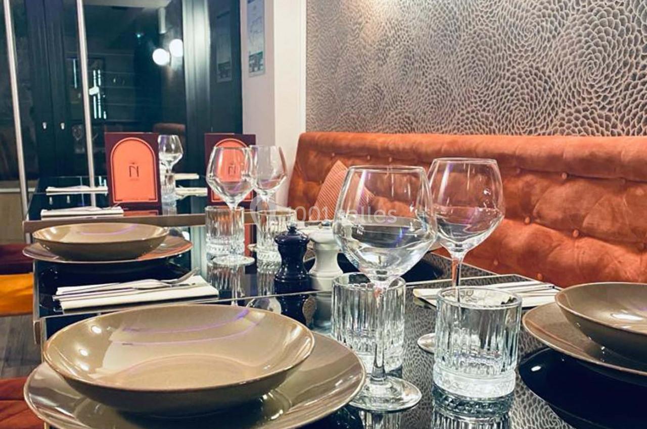 Table dressée dans un restaurant avec assiettes, verres et serviettes sur une table en verre, banquette orange en arrière…