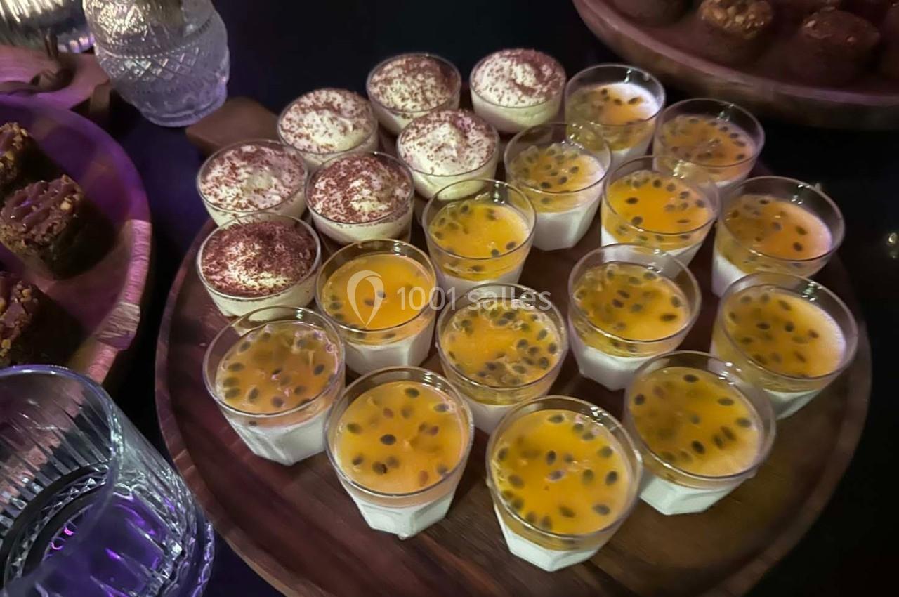 Plateau de verrines avec tiramisus saupoudrés de cacao et desserts au fruit de la passion, entouré de douceurs.