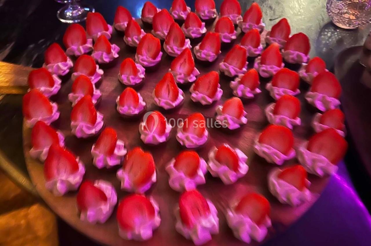 Plateau circulaire de bouchées garnies de fraises et de crème, présenté sur une table sombre.