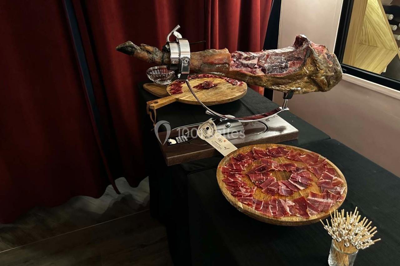 Jambon ibérique sur un support avec des assiettes de tranches fines disposées sur une table noire.