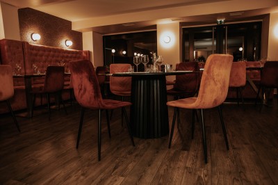 Salle de restaurant chaleureuse avec banquettes en velours rouge, chaises en bois et éclairage tamisé.