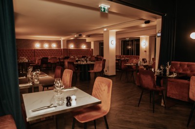 Salle de restaurant chaleureuse avec banquettes en velours rouge, chaises en bois et éclairage tamisé.