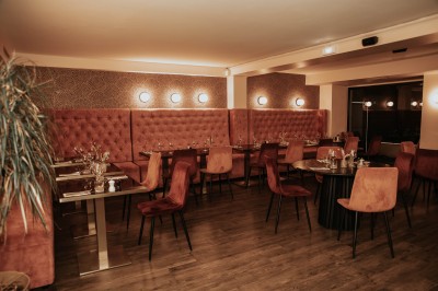 Salle de restaurant chaleureuse avec banquettes en velours rouge, chaises en bois et éclairage tamisé.