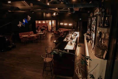 Salle de restaurant chaleureuse avec banquettes en velours rouge, chaises en bois et éclairage tamisé.