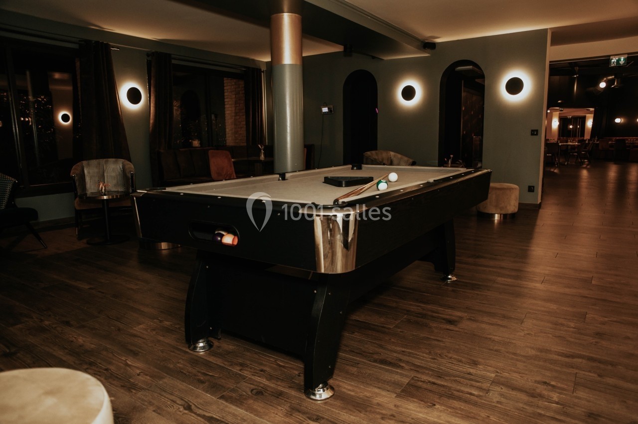 Table de billard noire avec accessoires, située dans une pièce au décor moderne et éclairage tamisé.