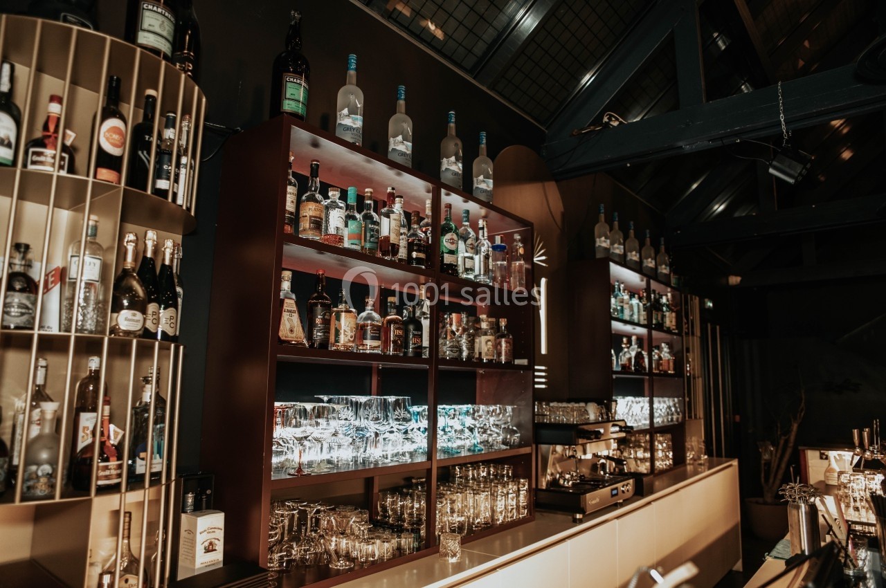 Étagères remplies de bouteilles d'alcool et de verres dans un bar à l'ambiance tamisée et moderne.