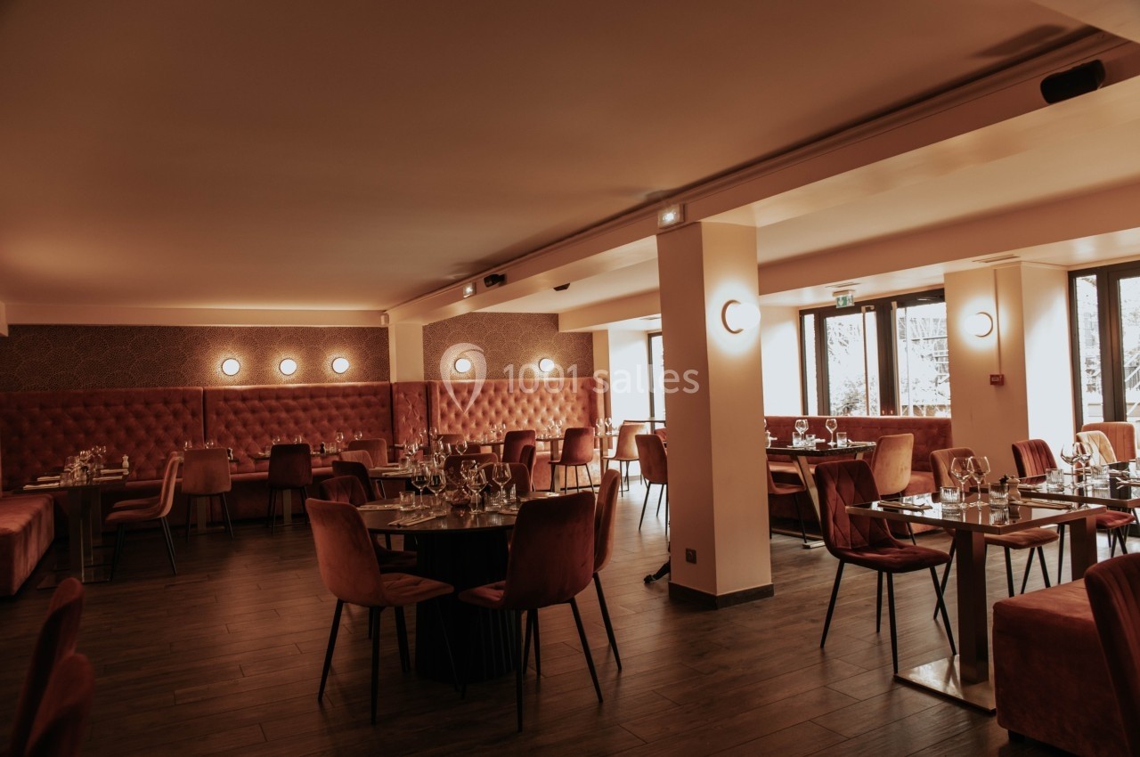 Salle de restaurant élégante avec tables dressées, chaises en velours et éclairage tamisé.