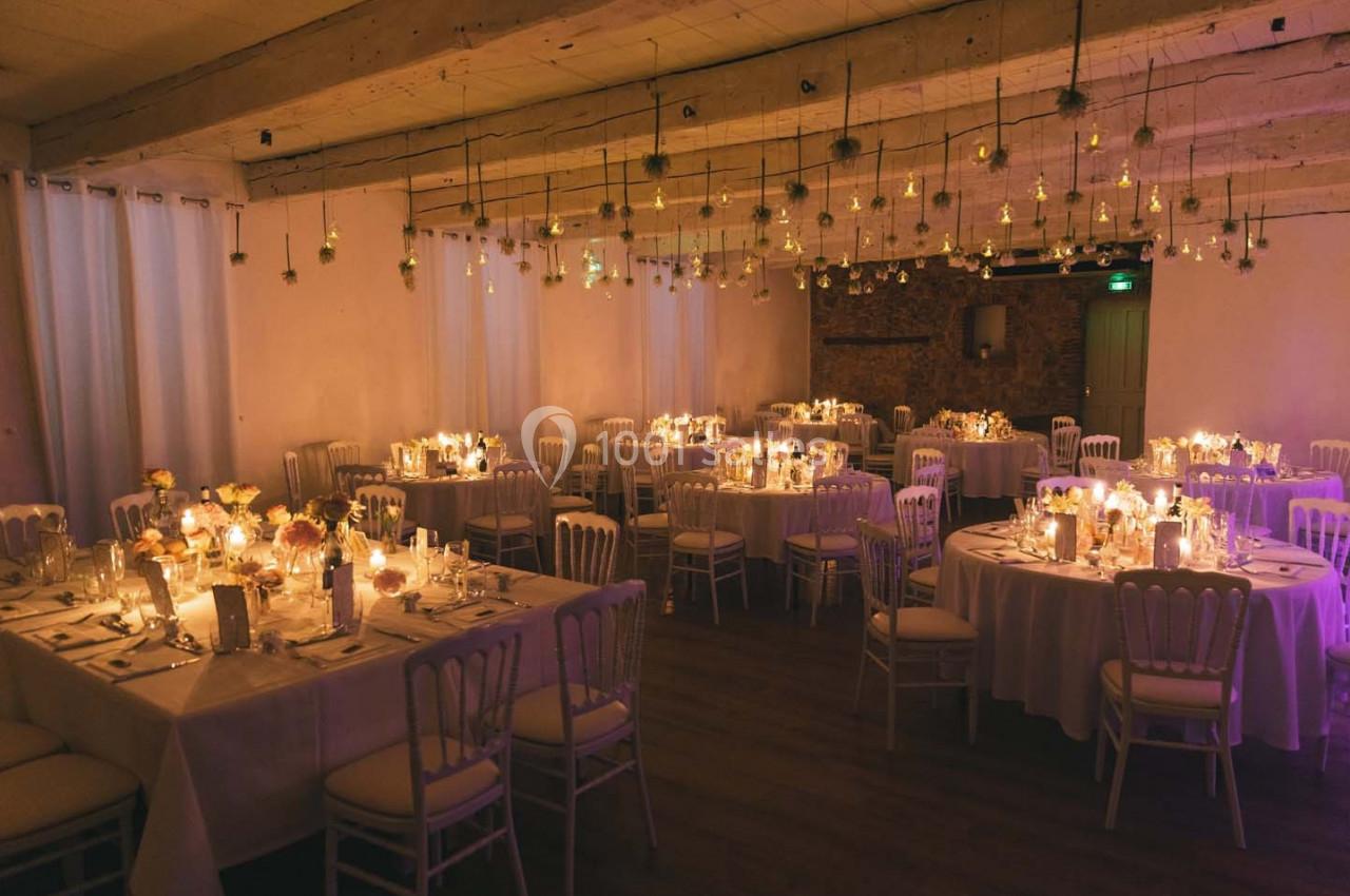 Salle de réception décorée avec des tables rondes, des bougies et des suspensions lumineuses dans une ambiance chaleureuse.