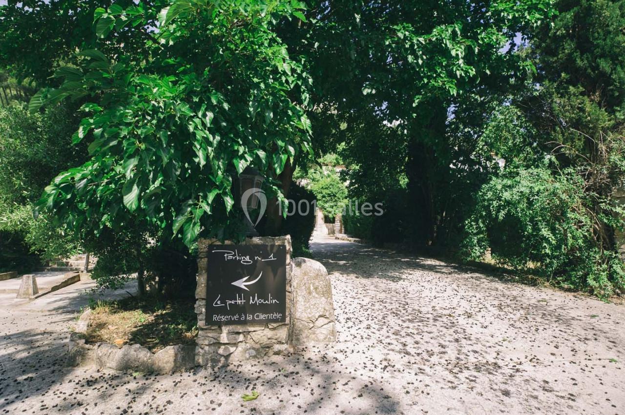 Chemin ombragé bordé de végétation dense avec un panneau indiquant ’Le petit Moulin, réservé à la clientèle’.