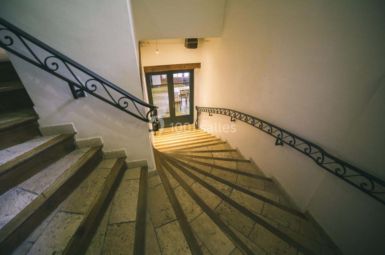 Escalier en pierre avec rampes en fer forgé, menant à une porte vitrée donnant sur l'extérieur.