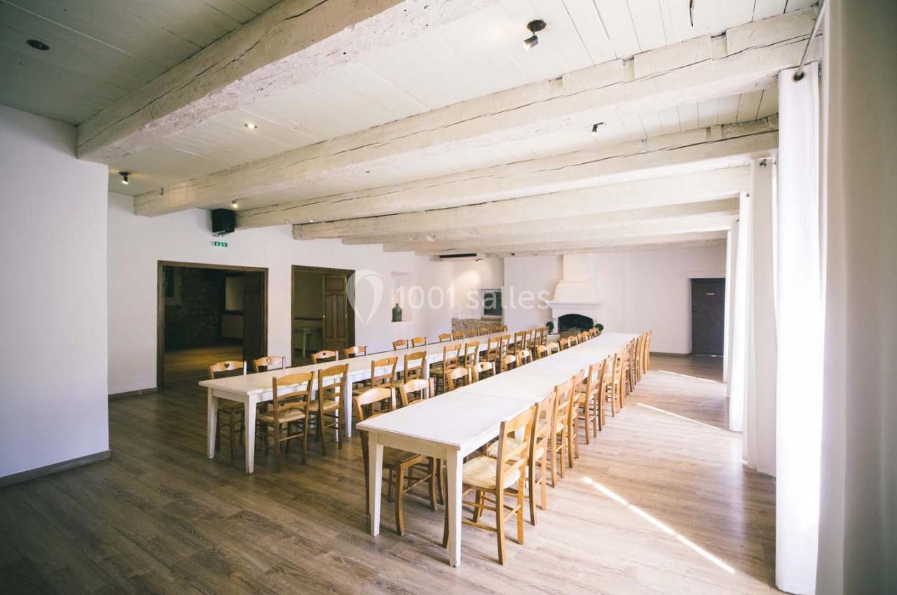 Salle lumineuse avec de longues tables en bois, des chaises assorties et un plafond avec poutres apparentes.
