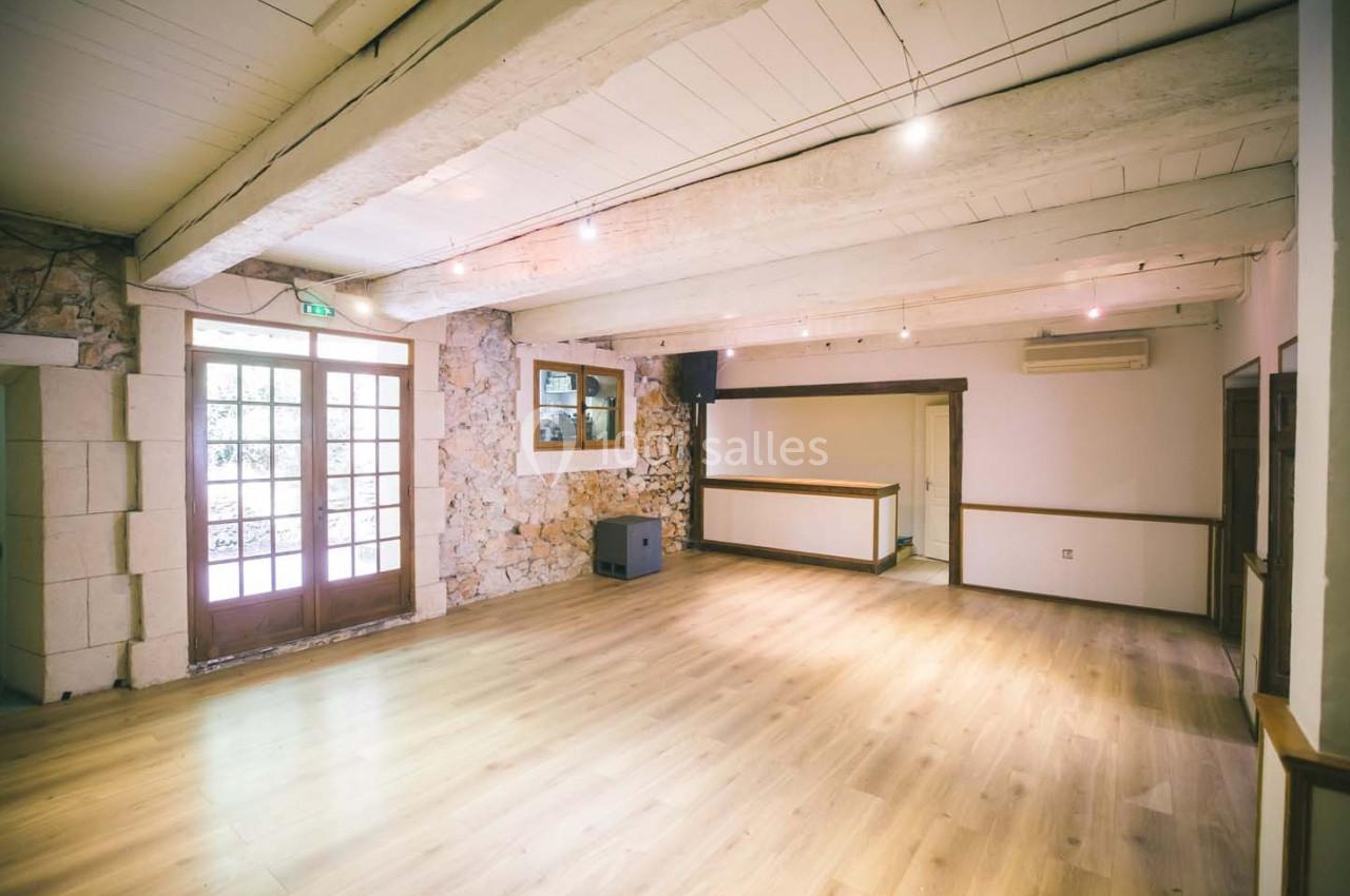 Salle lumineuse avec parquet en bois clair, murs en pierre et poutres apparentes, dotée de grandes portes vitrées.