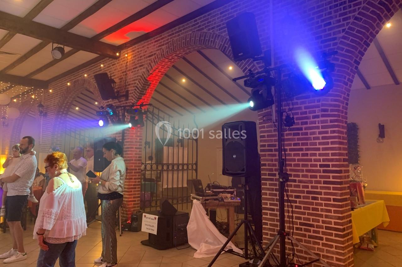 Salle de réception avec des invités debout, éclairages colorés et matériel de sonorisation près d'une arche en briques.