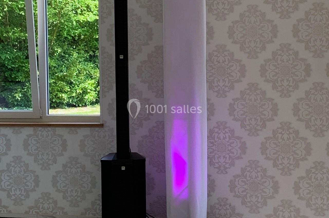 Colonne lumineuse avec éclairage violet et équipement audio à côté, installés dans une pièce lumineuse avec vue sur un…