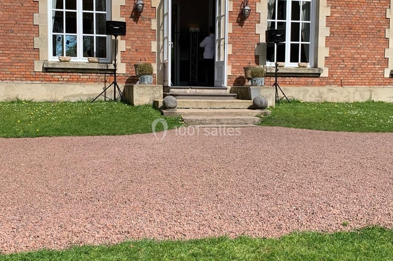 Façade d'un bâtiment en briques avec grandes fenêtres, porte ouverte et équipements audio installés à l'extérieur.