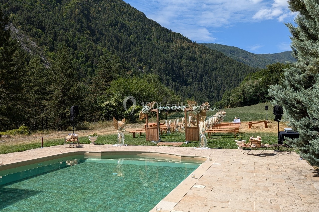 Vue d'une piscine entourée de montagnes, avec un espace de cérémonie en bois décoré dans un cadre naturel.