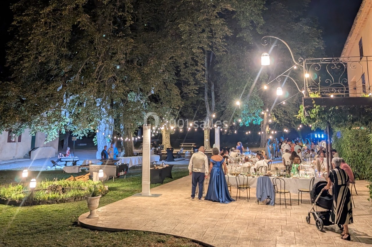 Dîner en plein air sous des guirlandes lumineuses, avec des invités élégants dans un jardin éclairé en soirée.
