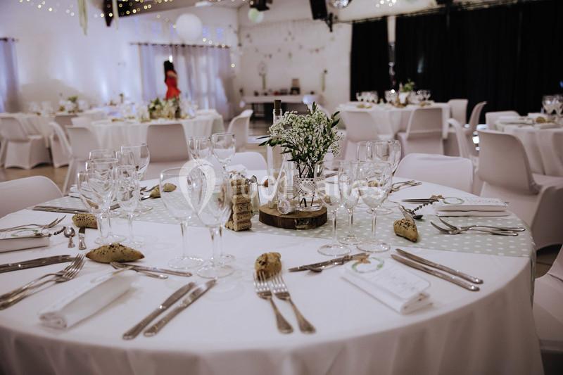 Tables élégamment dressées pour un événement, avec nappes blanches, verres, couverts et décorations florales.
