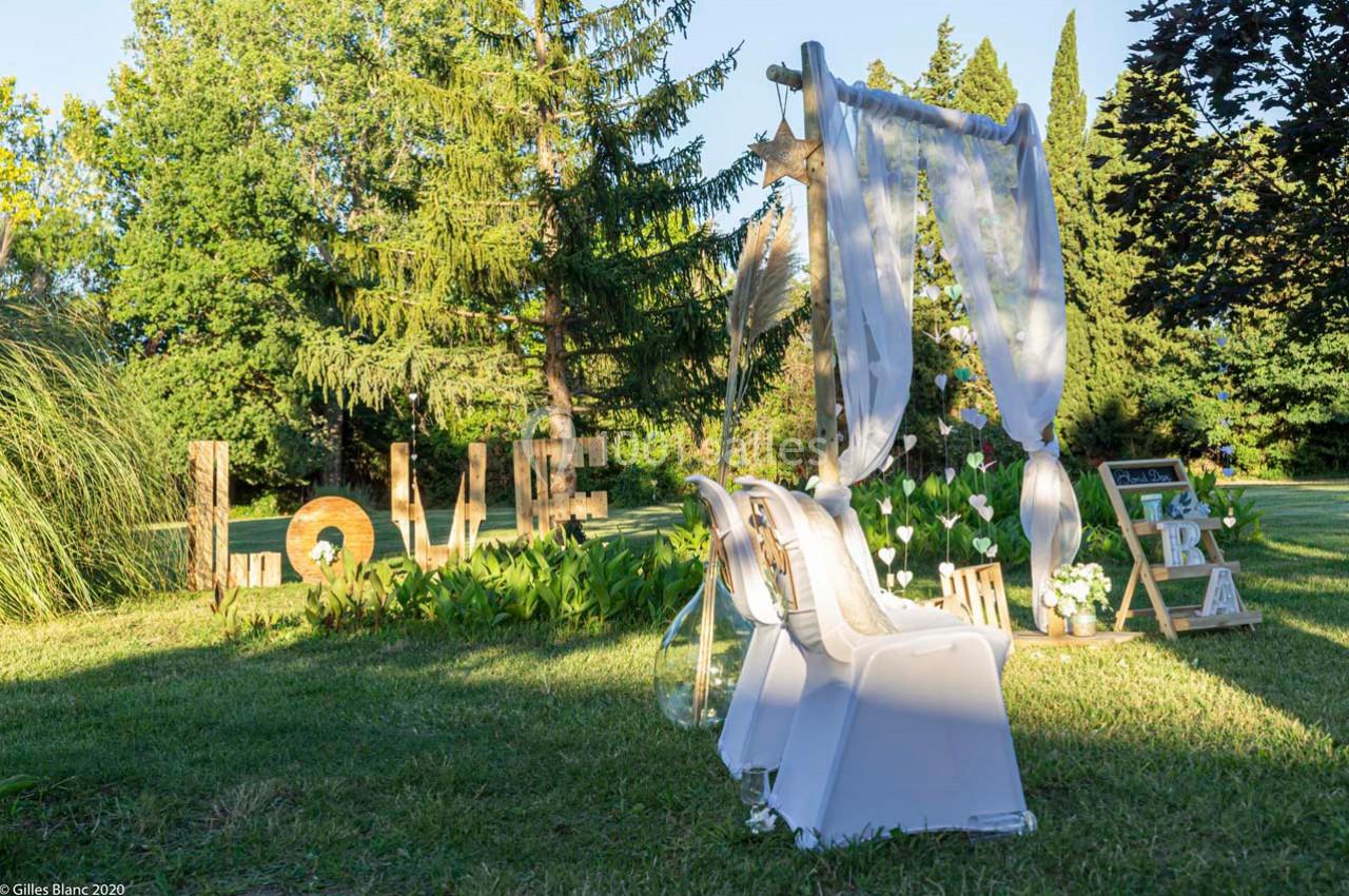Décoration de mariage en plein air avec arche blanche, chaises décorées et lettres en bois formant ’LOVE’ sur une pelouse.
