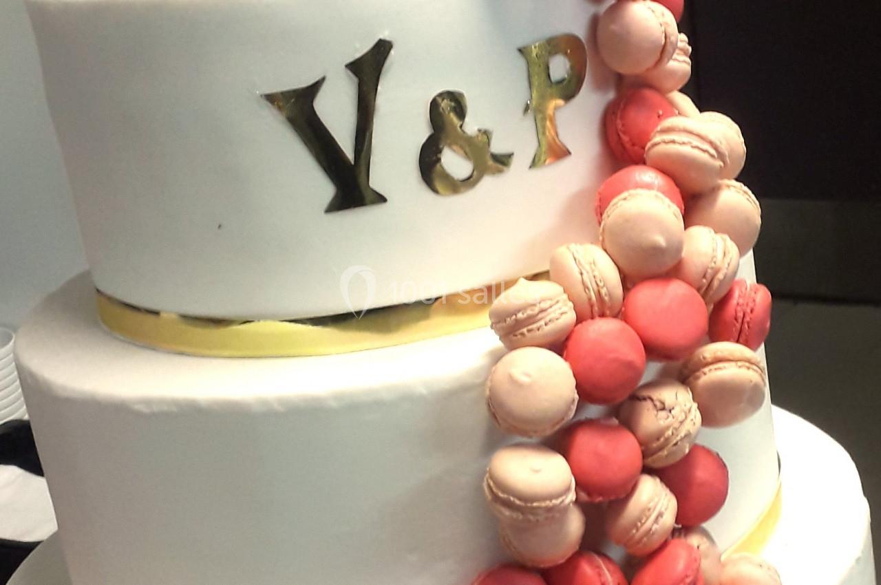 Gâteau de mariage à trois étages décoré de macarons roses et rouges, avec initiales dorées ’Y & P’.