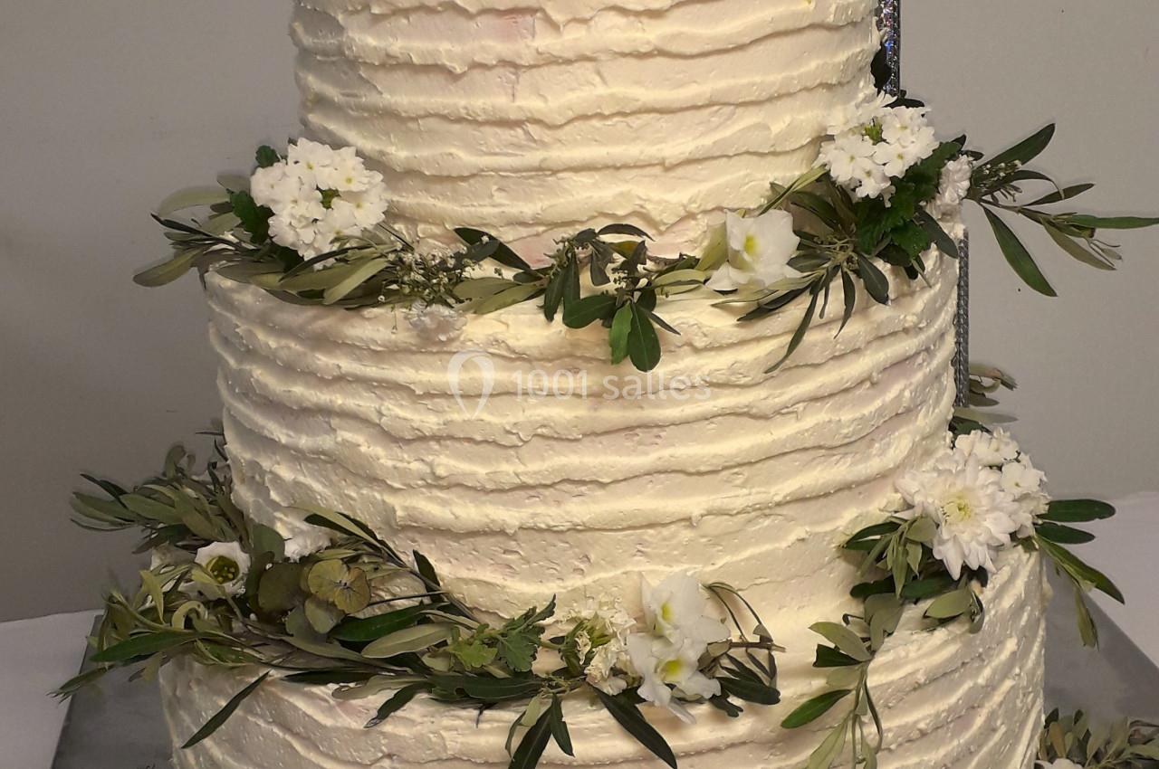 Gâteau de mariage à trois étages décoré de fleurs blanches, feuillages et roses crème au sommet.
