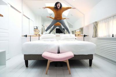 Lit avec oreillers blancs, lampe de chevet allumée et miroir reflétant une penderie et des portes dans une chambre lumineuse.