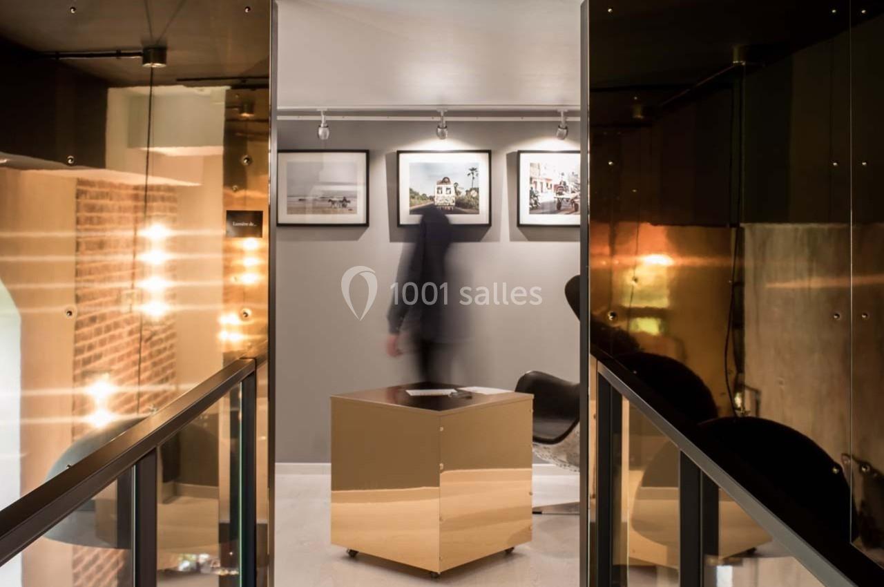 Un homme flou marche dans une galerie moderne avec des murs décorés de photos encadrées et des surfaces réfléchissantes.