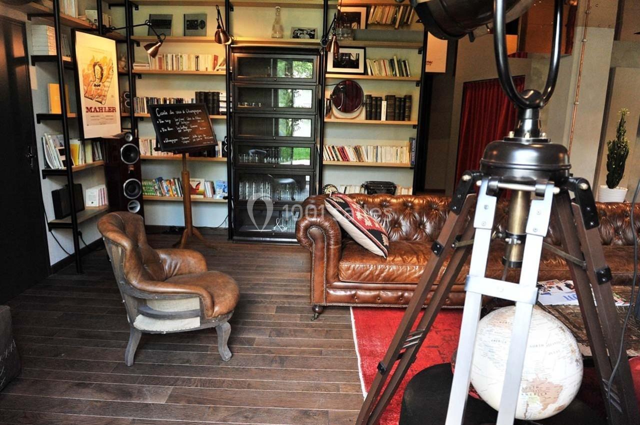 Salon chaleureux avec canapé en cuir, étagères remplies de livres, globe terrestre et projecteur vintage.