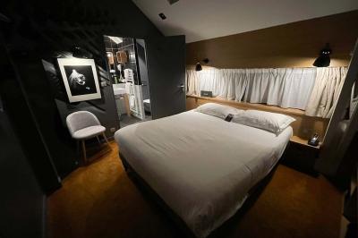 Lit avec oreillers blancs, lampe de chevet allumée et miroir reflétant une penderie et des portes dans une chambre lumineuse.